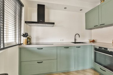 Çağdaş bir mutfak sahnesi. İçinde nane yeşili dolaplar, parlak aletler ve pencereden süzülen doğal ışık geniş bir atmosfer yaratıyor..