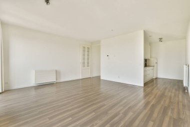 Geniş, modern, açık renkli duvarları ve ahşap zemini olan, açık mutfak alanı ile tamamlanmış boş bir oda. İç tasarım keşfi için ideal.