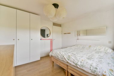 Yumuşak bir yatak örtüsü, beyaz mobilya ve doğal ışık içeren huzurlu bir minimalist yatak odası. Rahatlama ve sükunet için mükemmel..