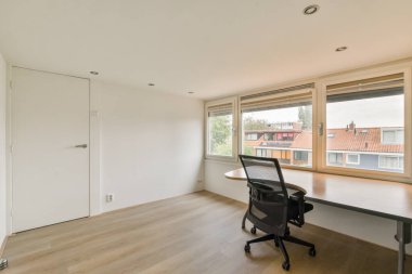 Geniş ve minimalist bir ofis içi. Doğal ışığın içeri girmesine izin veren geniş pencereler var. Açık ve davetkar bir atmosfer yaratıyor..
