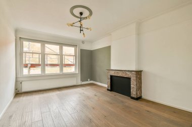 Temiz bir tasarımı olan şık ve minimalist bir oda, doğal ışığa izin veren geniş pencereler ve odak noktası olarak klasik bir şömine..