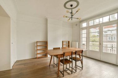 Büyük pencerelerden gelen doğal ışıkla aydınlatılmış ahşap masa ve sandalyelerin yer aldığı şık ve minimalist bir yemek odası..