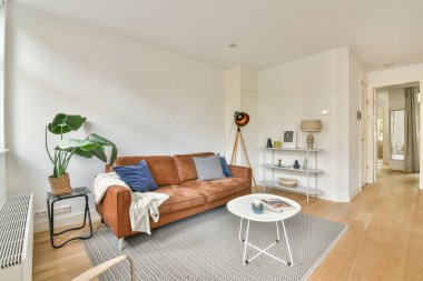 Şık bir modern oturma odası şık bir kanepe, kapalı salonda bitkiler, ahşap döşeme ve parlak doğal ışıklandırma, sıcak ve davetkar bir atmosfer yaratıyor..