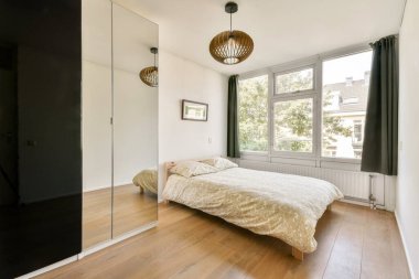 Çağdaş bir yatak odası, rahat bir yatak odası, geniş pencereler, doğal ışığa izin veren, ayna ve ahşap döşemeli şık bir dekor..