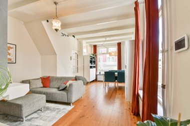 Konforlu gri bir kanepenin, ahşap zeminin ve zarif ışığın bulunduğu, sıcak ve davetkar bir atmosfer sunan çağdaş bir oturma odası. Rahatlama ve toplanma için mükemmel..