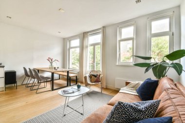 Modern mobilyaların, büyük pencerelerin ve doğal ışık ve yeşilliğin karışımının yer aldığı parlak ve havadar bir oturma odası hoş bir atmosfer yaratıyor..
