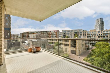 Geniş bir balkon çağdaş bir şehir manzarasını gözler önüne seriyor, cam korkuluklar ve saksı bitkileriyle süslenmiş sakin bir açık alan..