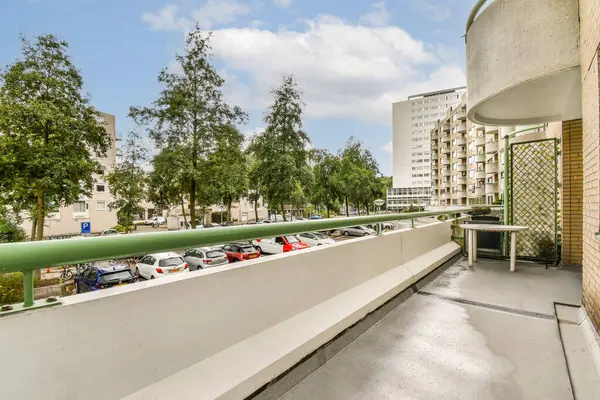 Çağdaş bir balkon, açık gökyüzü altındaki ağaçların ve kentsel binaların manzarasını sergiliyor. Rahatlamak ve dışarıda eğlenmek için mükemmel..