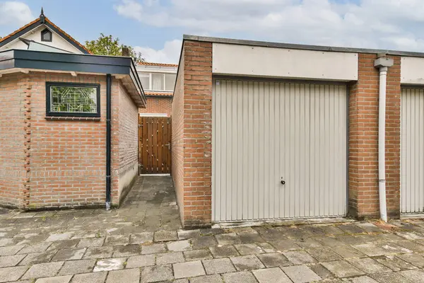 Modern bir garaj kapısını, tuğladan bir binanın yanında, üzerinde temiz bir gökyüzü ve önünde düzgün asfalt bir yol olan bir manzara..