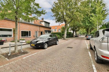 Ağaçlarla ve park edilmiş araçlarla dolu sakin bir yerleşim yeri manzarası yeşil ve modern şehir yaşamının bir karışımını sergiliyor..