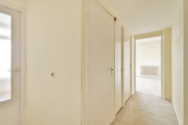 Bu resim açık renkli duvarları ve kapıları olan ferah ve minimalist bir iç koridor sergiliyor, basitlik ve zarafeti vurguluyor..