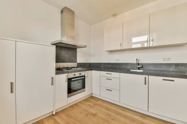 Çağdaş mutfak, gösterişli beyaz dolap, paslanmaz çelik eşyalar, ahşap döşemeler, minimalist estetik ve işlevsel bir düzen sergiliyor..