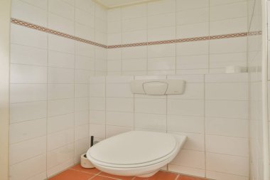 Beyaz fayanslı duvarlara karşı modern bir tuvaletin olduğu temiz ve basit bir banyo, ince bir sınır tasarımı ile vurgulanmış. Fonksiyonel ve dağınık boşluk.