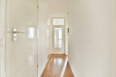 Beyaz duvarları ve ahşap döşemeleri olan ferah, parlak bir koridor. Minimalist tarzda tasarlanmış ve atmosferi güçlendiriyor..