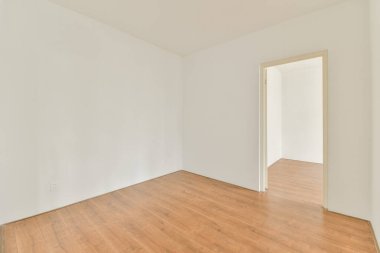 Ahşap zemin ve başka bir odaya açılan bir kapı olan ferah, boş bir oda. Duvarlar sade ve sade, minimalist bir estetik sağlıyor..