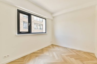 Geniş pencereli minimalist bir oda doğal ışığın boşluğu doldurmasına izin veriyor, zarif ringa kemiği döşemeleri ve duvarların temiz çizgilerini sergiliyor..