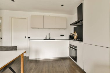 Şık ve işlevsel bir mutfak. Beyaz dolaplı ve modern aletli modern bir tasarım. Organize bir yemek alanı yaratıyor..