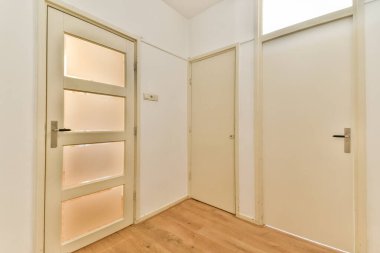 Temiz ve minimalist estetiğe sahip iki kapalı kapının bulunduğu çağdaş bir koridor. Açık ahşap döşeme nötr duvar renklerini tamamlıyor..