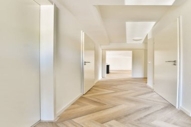 Minimalist bir iç koridor pürüzsüz beyaz duvarlar ve geniş ve havadar bir atmosfer yaratan zarif ahşap döşemeler sergiliyor..