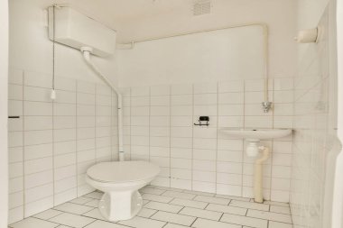 Beyaz fayanslı duvarları, tuvaleti ve minimalist estetiği destekleyen küçük bir lavabosu olan modern bir banyonun gösterişli ve temiz bir tasarımı..
