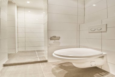 Çağdaş bir banyo, parlak beyaz fayanslar, modern bir tuvalet ve minimalist bir estetik. Geniş tasarım temizlik ve zarafeti vurguluyor..