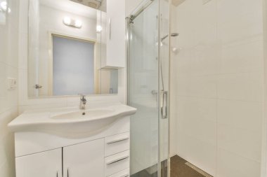 Pürüzsüz ve çağdaş bir banyo tasarımı, cam duş muhafazası, şık bir lavabo, ve temiz beyaz fayanslar, havadar ve minimalist bir estetiği teşvik eden.