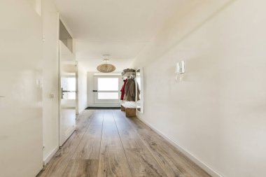 Geniş ve minimalist koridorda açık renkli duvarlar, ahşap döşemeler ve şık bir aydınlatma armatürü var. Tasarım, çağdaş estetiği ve basitliği yansıtıyor..