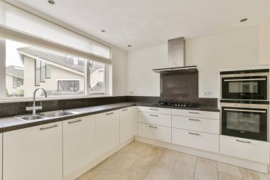 Gösterişli beyaz dolaplar, siyah bir tezgah ve yemek pişirmek ve toplamak için işlevsel bir alan yaratan modern mutfak..