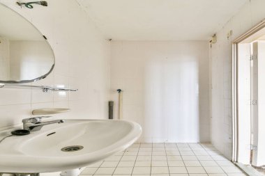 Minimalist modern banyo. Beyaz lavabosu, aynası ve fayanslı zemini var. Işık, uzayın temiz ve ferah hissini arttırır..