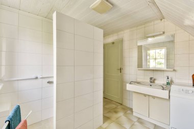 Parlak ve temiz bir modern banyo fayansla döşenmiş duvarlar, bir lavabo ve bir duş alanı, bir pencereden gelen doğal ışıkla aydınlatılmış..