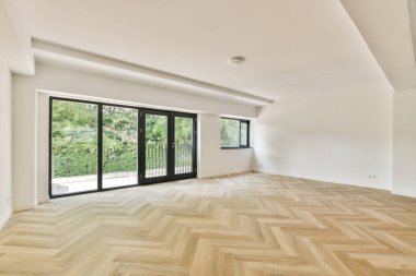 Geniş pencereli, geniş doğal ışık getiren, güzel ahşap döşemeleri ve minimalist tasarım elementlerini sergileyen geniş bir oda..