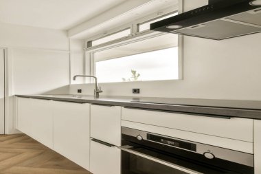 Minimalist dolap şiirleri, şık bir lavabo ve büyük pencerelerden içeri akan doğal ışığın yer aldığı gösterişli bir modern mutfak davetkar bir atmosfer yaratıyor..