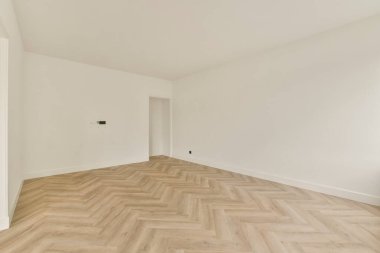 Geniş, minimalist bir iç mekan. Açık renkli bir duvar ve ringa kemiği ahşap döşeme. Modern yaşam alanları için ideal..