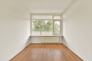 Geniş, minimalist bir iç oda, ahşap döşeme ve geniş pencereler, doğal ışığın içeri akmasına izin vererek, huzurlu bir atmosfer yaratıyor..