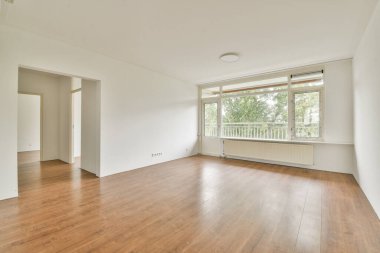 Ahşap döşemeleri ve geniş pencereleri olan modern, boş bir oturma odası geniş doğal ışığa izin veriyor, hoş bir atmosfer yaratıyor..