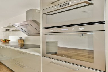 Çağdaş bir mutfak tasarımı, dahili aletler, minimalist dolaplar ve zarif ahşap zemin. Fonksiyonellik ve stile vurgu.