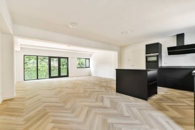 Geniş, modern bir mutfak ve yemek alanı. Parlak siyah dolaplar ve doğal ışığın odayı doldurarak minimalist estetiğini geliştirmesine olanak sağlayan geniş pencereler..