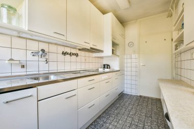 Parlak beyaz dolaplar, paslanmaz çelik aletler ve minimalist tasarım içeren çağdaş bir mutfak, yemek pişirmek için temiz ve işlevsel bir alan sunar..