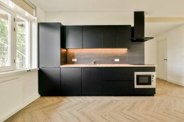 Gösterişli ve çağdaş bir mutfak. İçinde karanlık dolaplar, minimalist aletler ve sıcak ışıklandırma var. Modern yaşam alanları için mükemmel..
