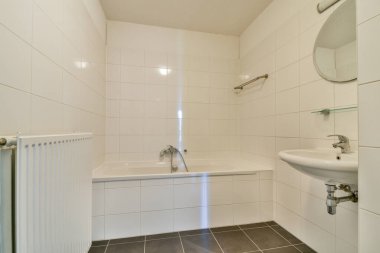 Beyaz fayanslı duvarlar, küvet ve modern eşyalar olan gösterişli, modern bir banyo. Minimalist tasarım boşlukları, temizliği ve basitliği arttırır..