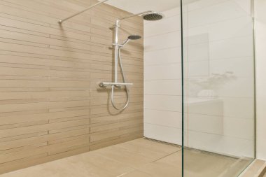 Pürüzsüz, minimalist, nötr renkli fayanslar ve cam kaplamalı, açık ve davetkar bir atmosfer yaratan şık bir duş alanı..