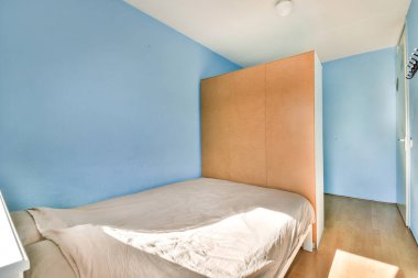 Açık mavi duvarlar, ahşap bölme ve yumuşak doğal ışıklandırmayla rahatlamak için sakin bir atmosfer yaratan minimalist bir yatak odası..