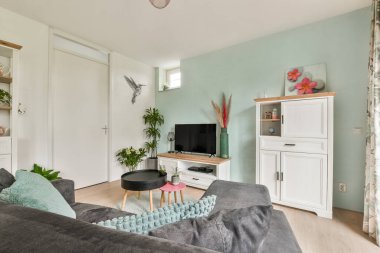 Parlak ve şık bir oturma odası rahat bir kanepe, dekoratif bitkiler ve mekanın atmosferini yükselten modern dekoratif elementler..