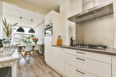 Güzel tasarlanmış modern mutfak vitrinleri, parlak dolaplar paslanmaz çelik aletler ve doğal ışıkla aydınlatılmış rahat bir yemek alanı..