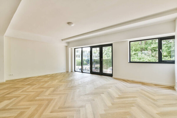 Светлое и просторное внутреннее пространство с деревянным полом из сельди и большими окнами, которые приглашают солнечный свет, создавая уютную атмосферу.