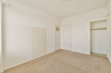 Geniş, dağınık, açık renkli duvarları, halılı zemini ve basit bir dolabı olan bir oda. İç tasarım ilhamı ya da gayrimenkul listesi için ideal.