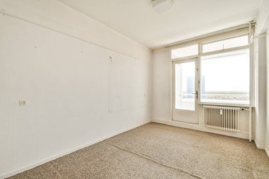 Geniş, minimalist, boş bir oda. İçinde doğal ışığın içeri girmesini sağlayan geniş pencereler var. Huzurlu bir atmosfer yaratıyor. Duvarlar beyaz, havayı geliştiriyor..