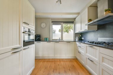 Beyaz dolaplar, ahşap döşemeler ve şık aletlerle donatılmış şık, modern bir mutfak yemek ve yemek pişirmek için parlak ve ferah bir atmosfer sağlıyor..