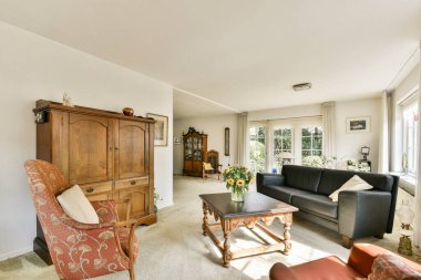 Zarif ahşap mobilyaların bulunduğu şık bir oturma odası, rahat bir oturma alanı ve geniş pencerelerden akan doğal ışık sıcak bir atmosfer yaratıyor..