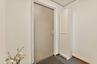 Kapalı bir kapı ve tarafsız bir duvara karşı basit bir depolama ünitesinin yer aldığı modern ve minimalist bir iç koridor..